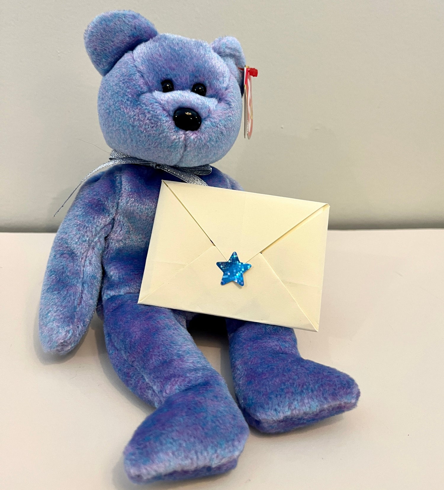 Blue beanie baby holding a tiny letter.
